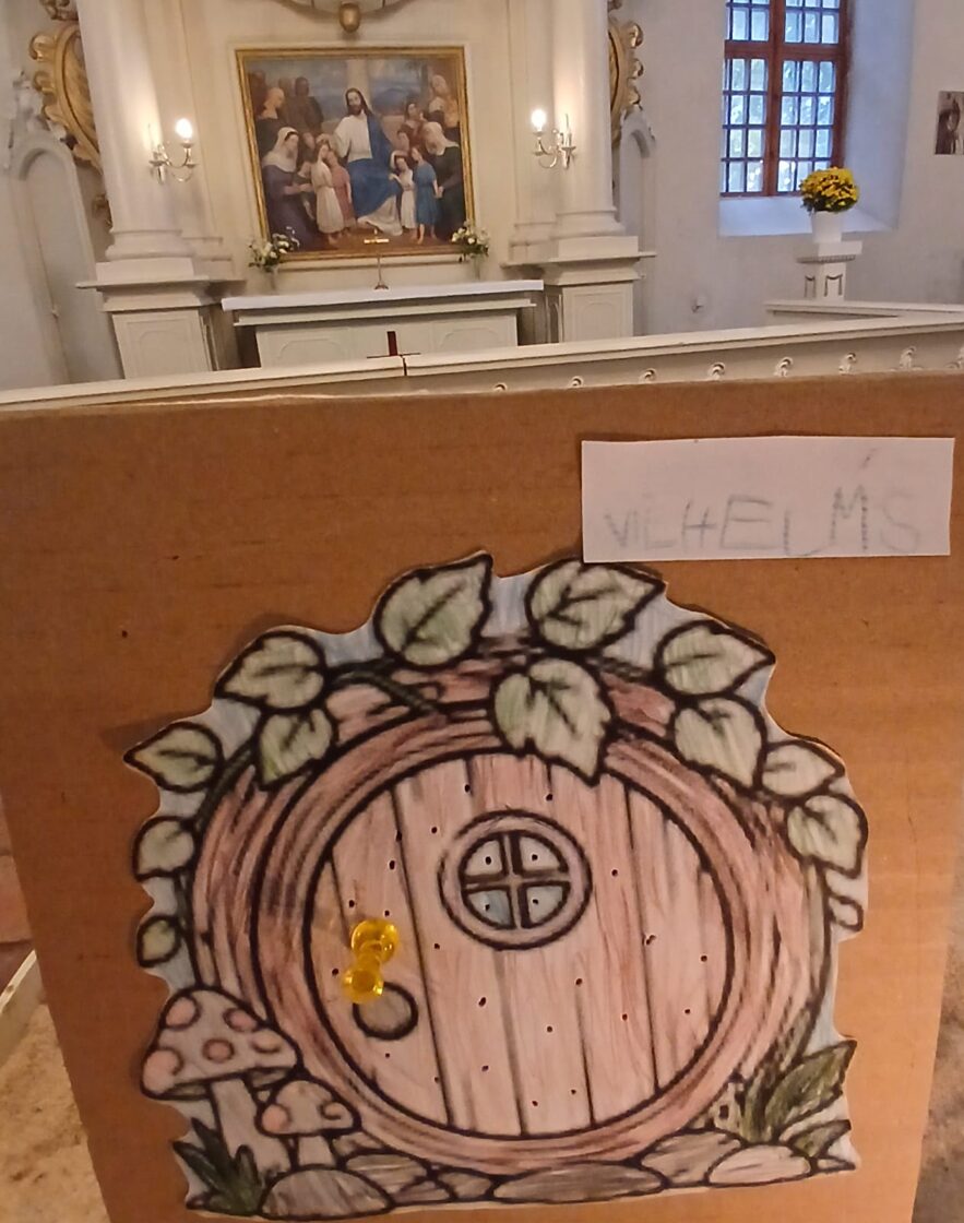 Svētdienas skolas nodarbībā izkrāsotas papīra durvis ar caurumiem pie altāra Liepupes baznīcā